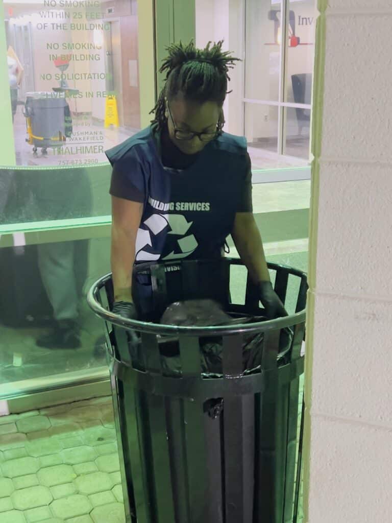 Day porter emptying a trash can in an office setting.