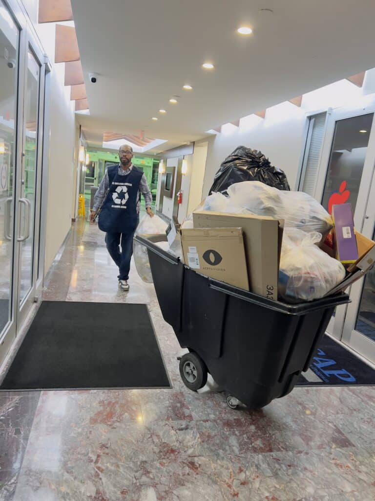 General Janitorial Photo of a LEL janitor with a large bin of trash to throw away in an office building setting.