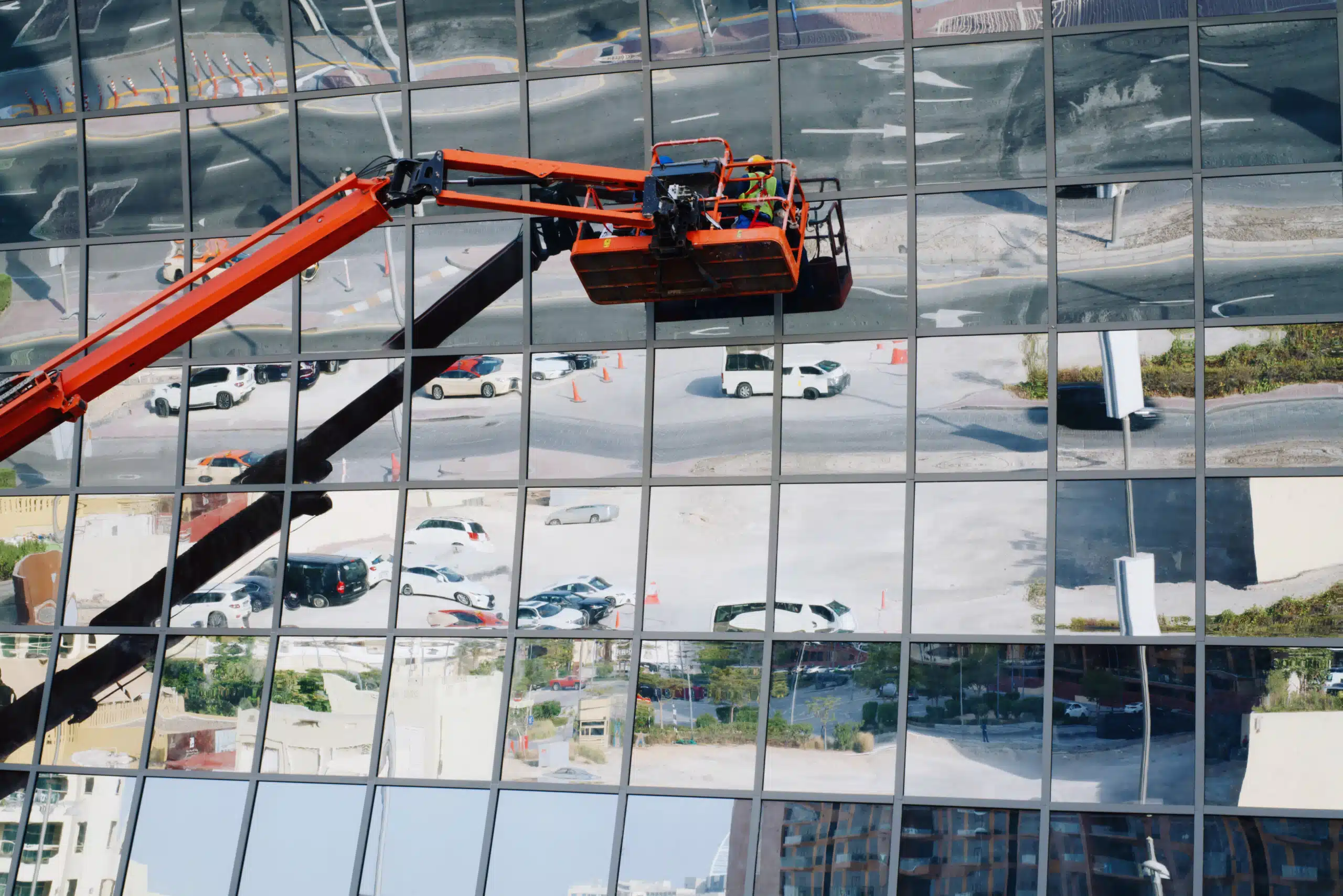People cleaning windows outside a commercial glass building using a crane lift with bucket.